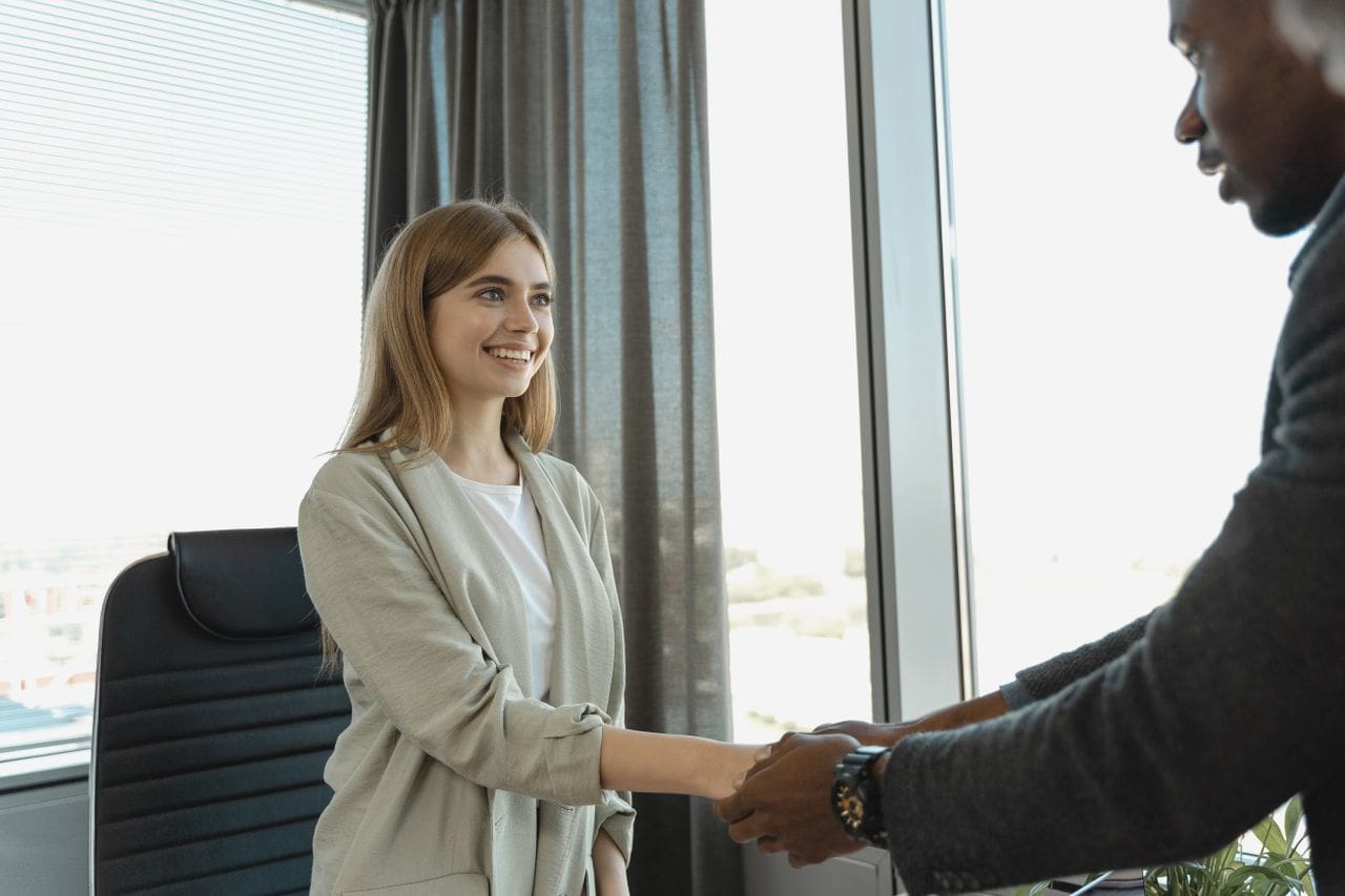 journey Woman smiling and shaking hands at a business office, signaling a successful job interview.